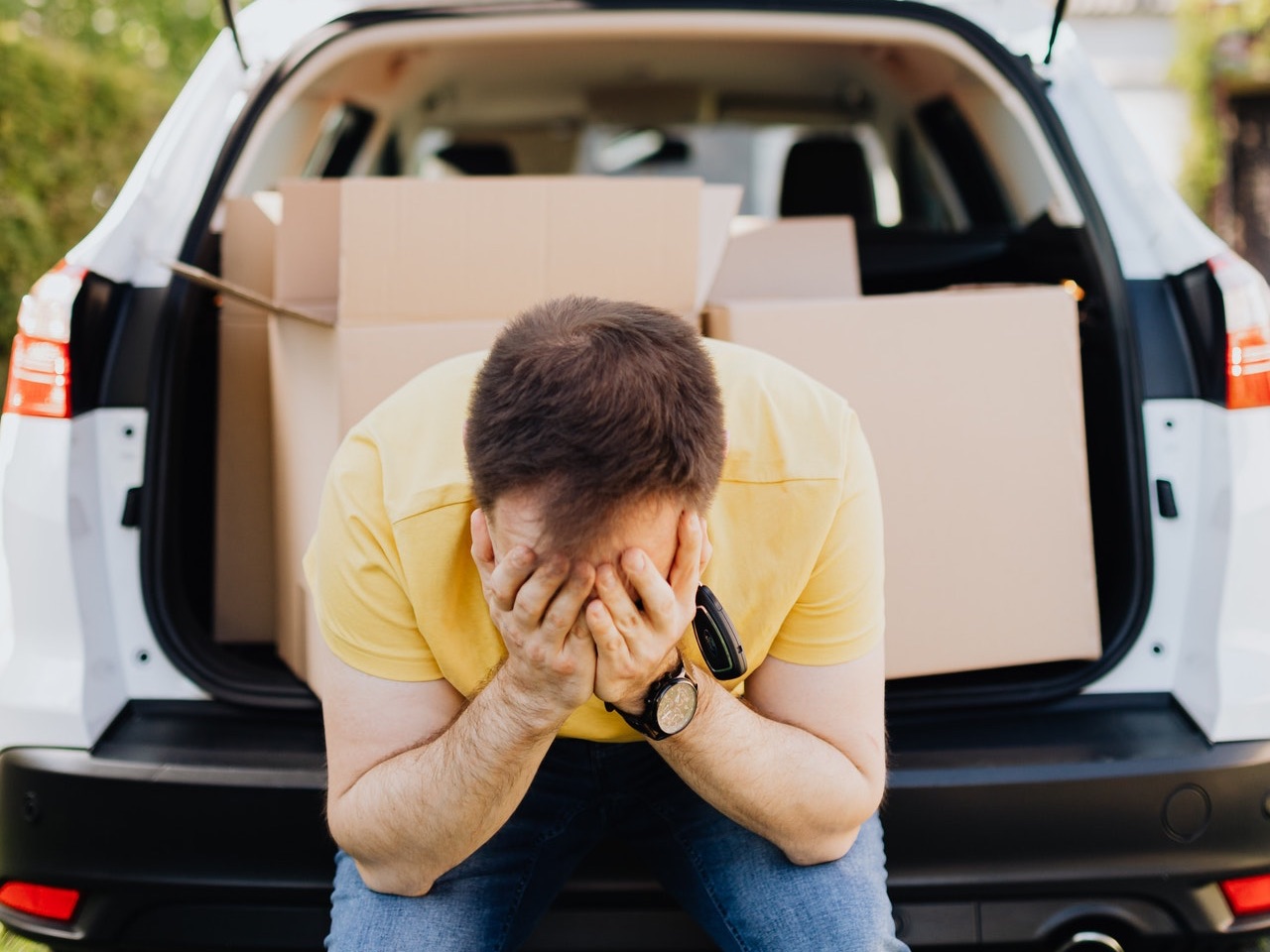 Foto de homem sentado no porta-malas do carro, com caixas de mudança atrás