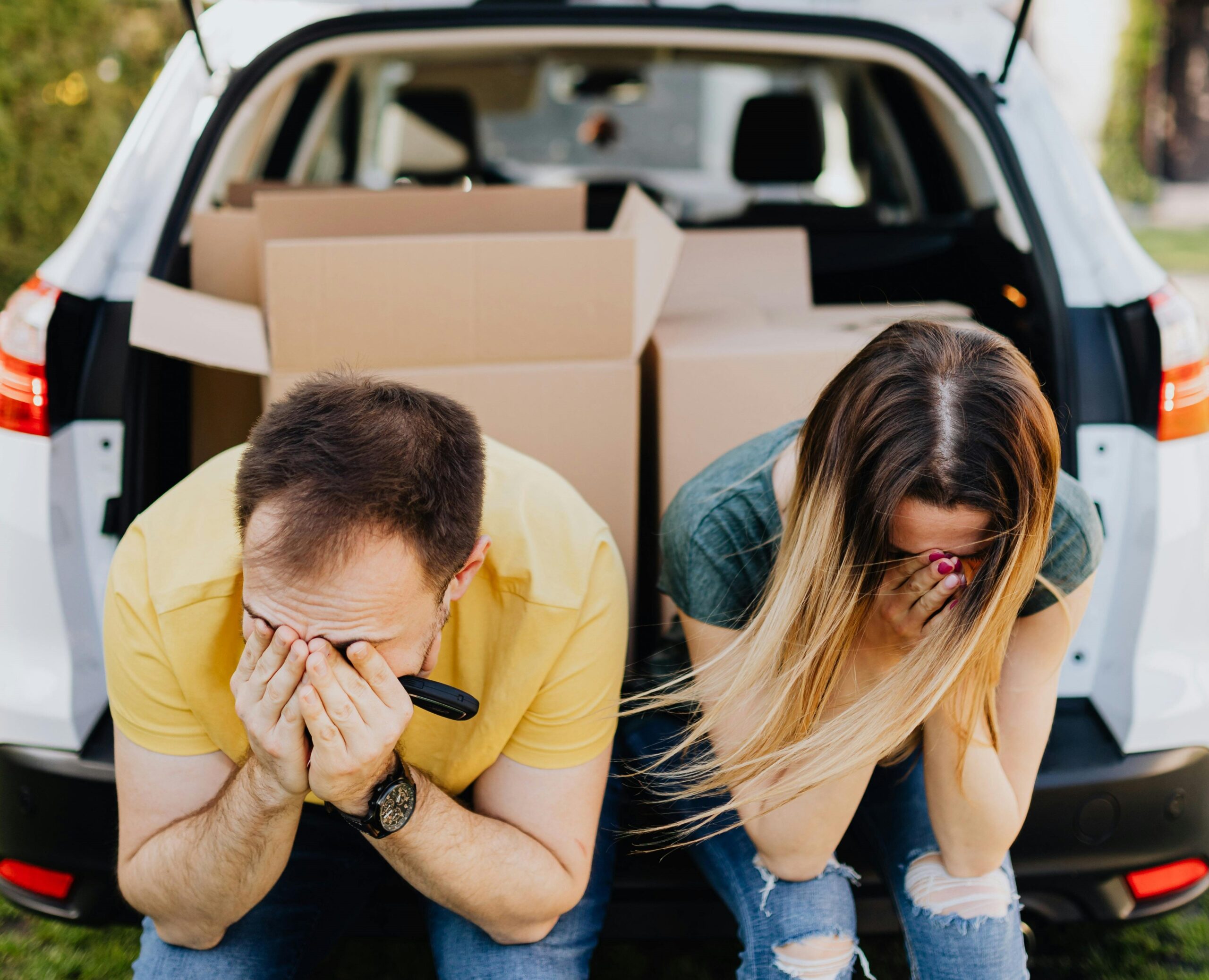 Casal com as mãos ao rosto, sentado sobre o porta-malas do carro cheio de caixas, lamentando uma ação de despejo por falta de pagamento